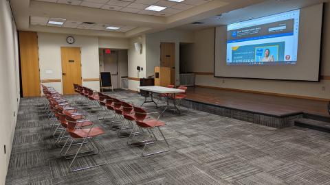 Linda Sickles Meeting Room A with stage, podium, table, projector and screen, and 20 chairs.