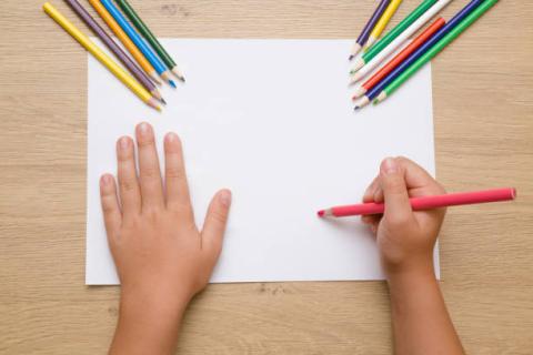 Child's hands drawing with colored pencils on white paper.