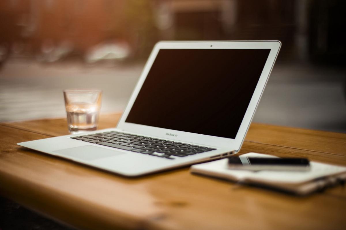image of a laptop, glass of water, a pen and a notebook on a table